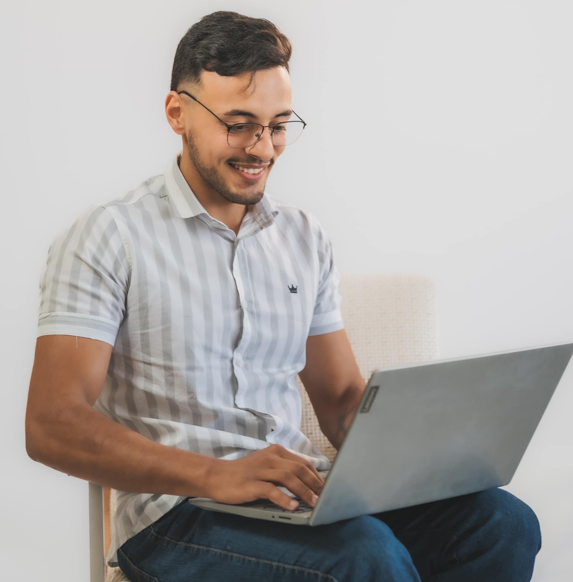 jovem de óculos e camisa de botões estuda sorridente para a redação em um notebook